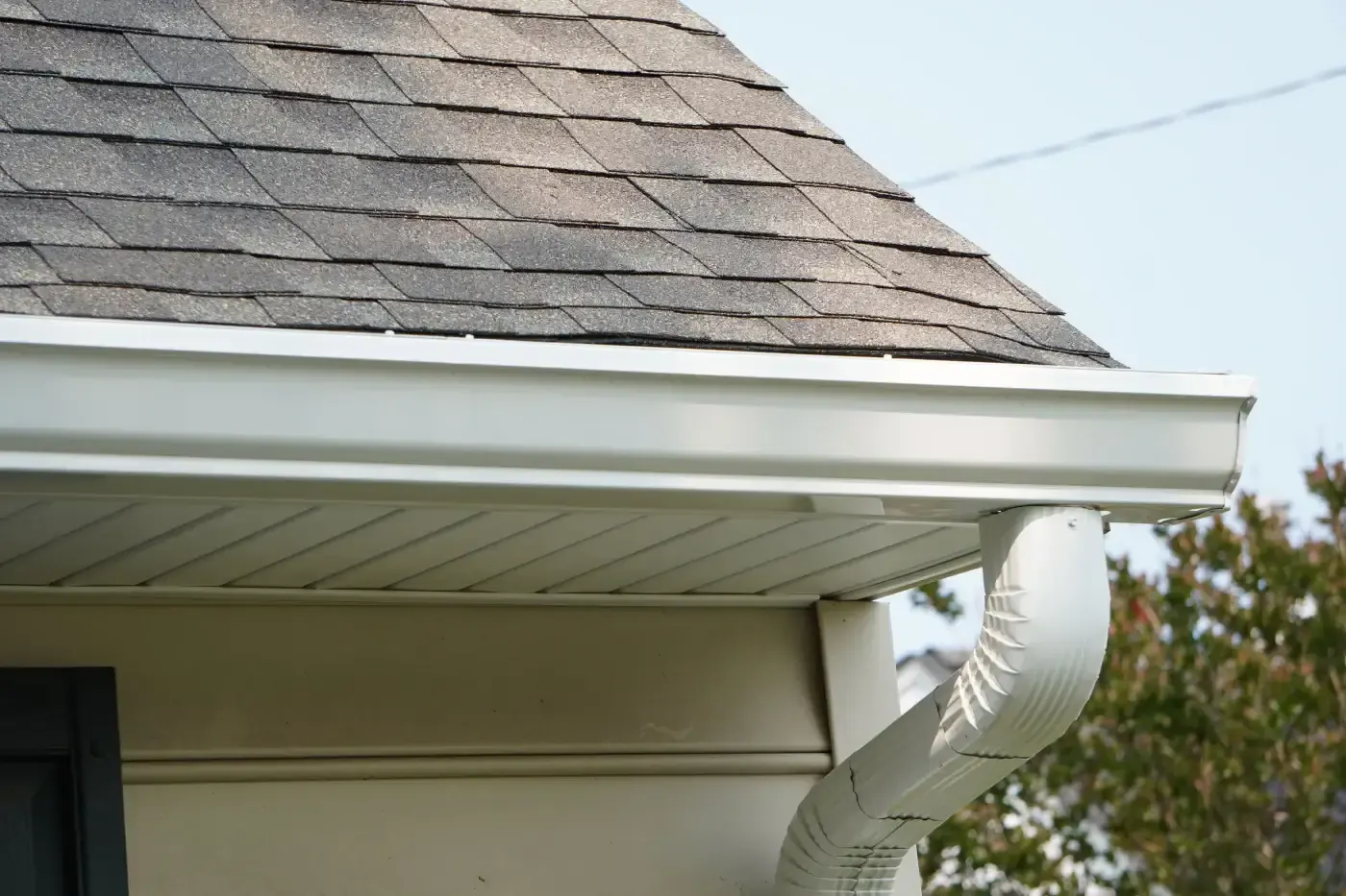White gutter with curved downspout beneath a residential eave