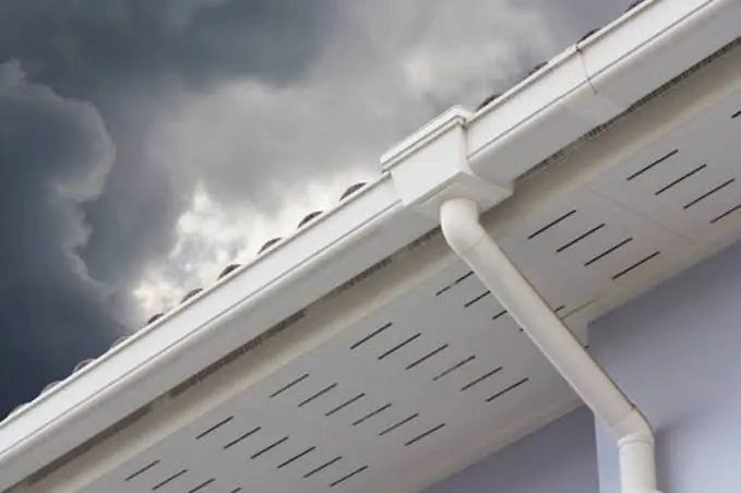 White gutter and downspout beneath dark storm clouds