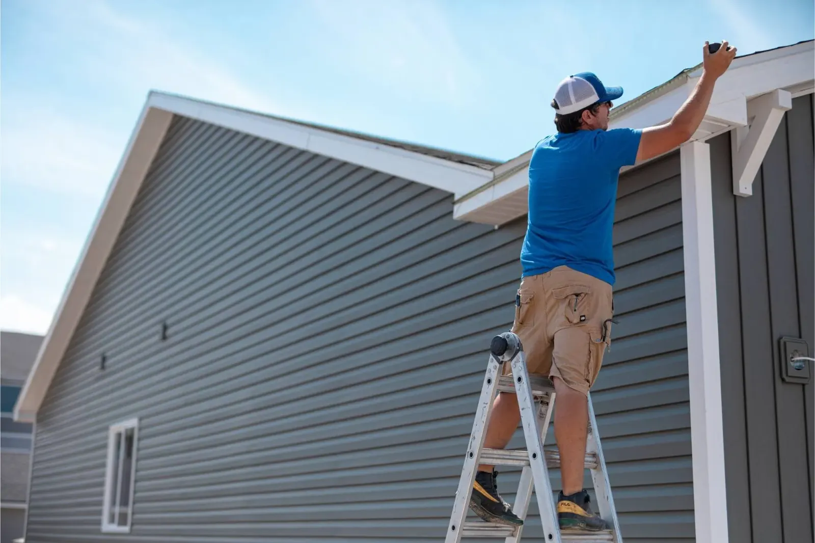 Worker measuring a residential roof edge from a ladder