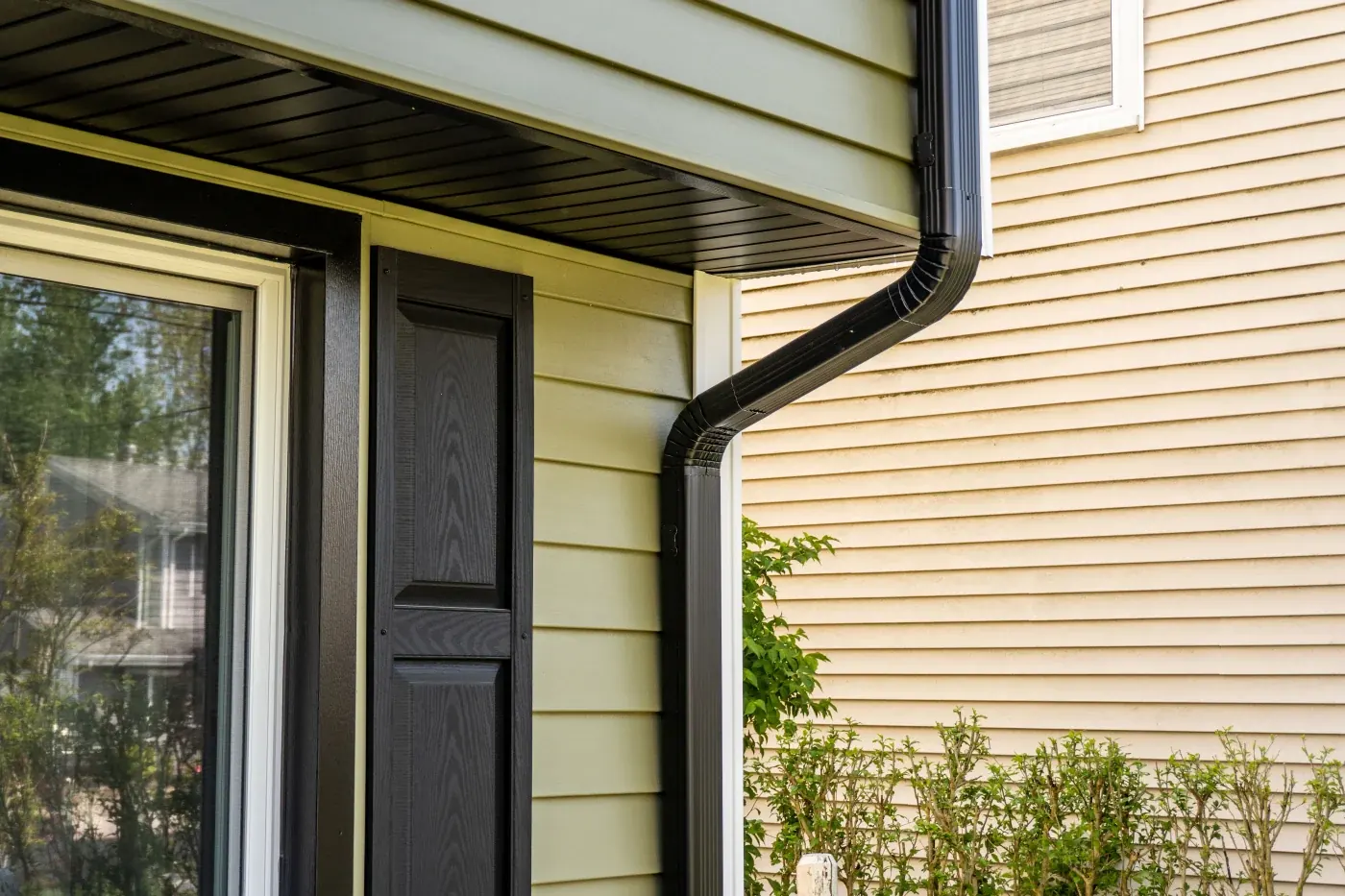Black downspout routed beside a window on light siding