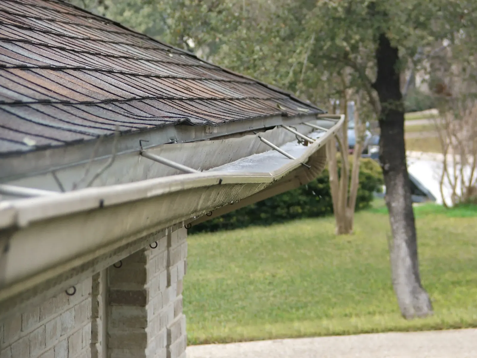 Bent sagging gutter with debris along an aging roof